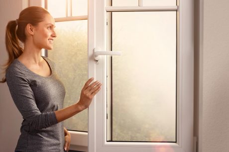 Frau sieht aus einem Kunststoff-Fenster nach draußen